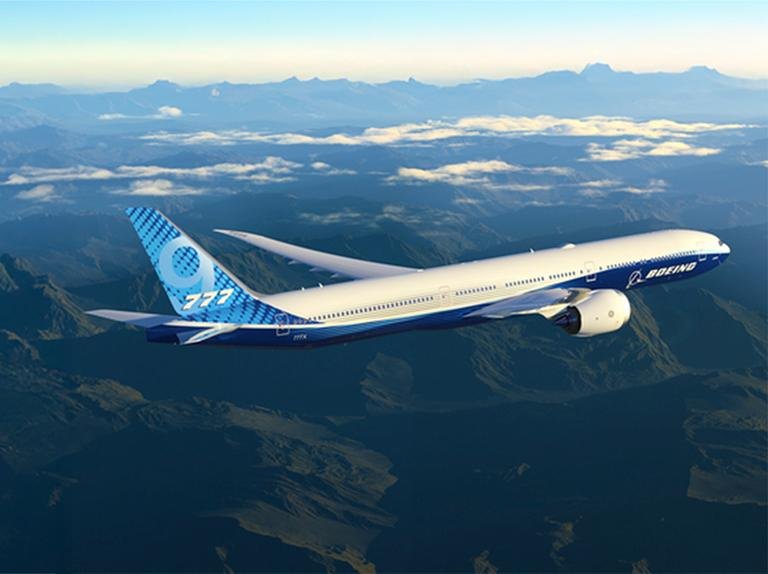 Boeing 777-9 flying over mountains, showcasing its folding wingtips and GE9X engines