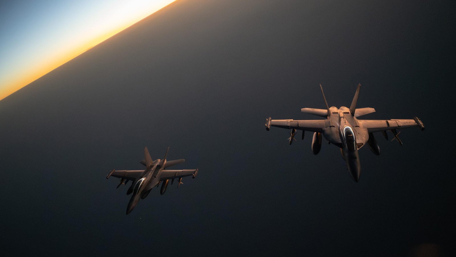 Two EA-18G Growlers flying in formation at sunset with wingtip ALQ-218 receiver pods visible