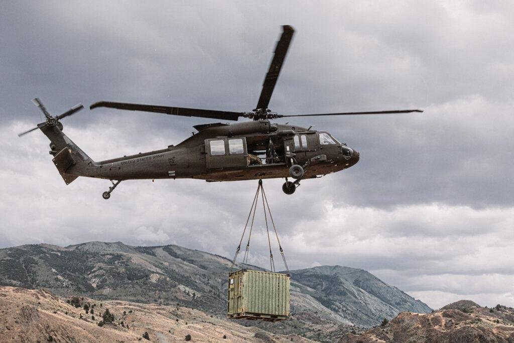 U.S. Army UH-60L Black Hawk lifts Marines and a cargo container during external load training in a mountain valley