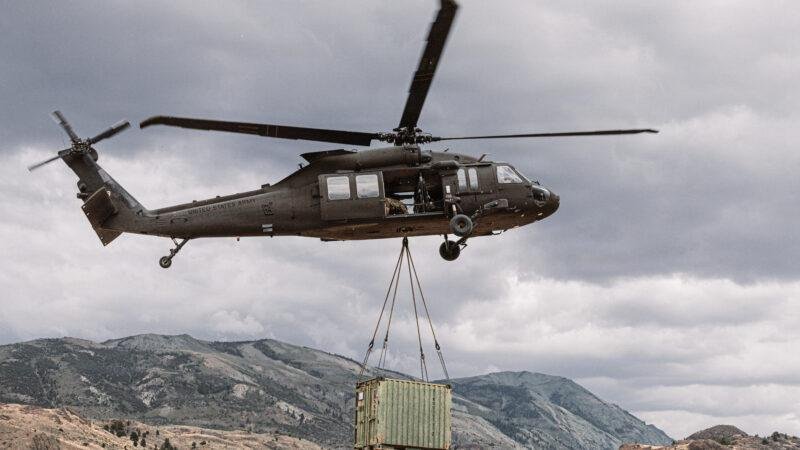 U.S. Army UH-60L Black Hawk lifts Marines and a cargo container during external load training in a mountain valley