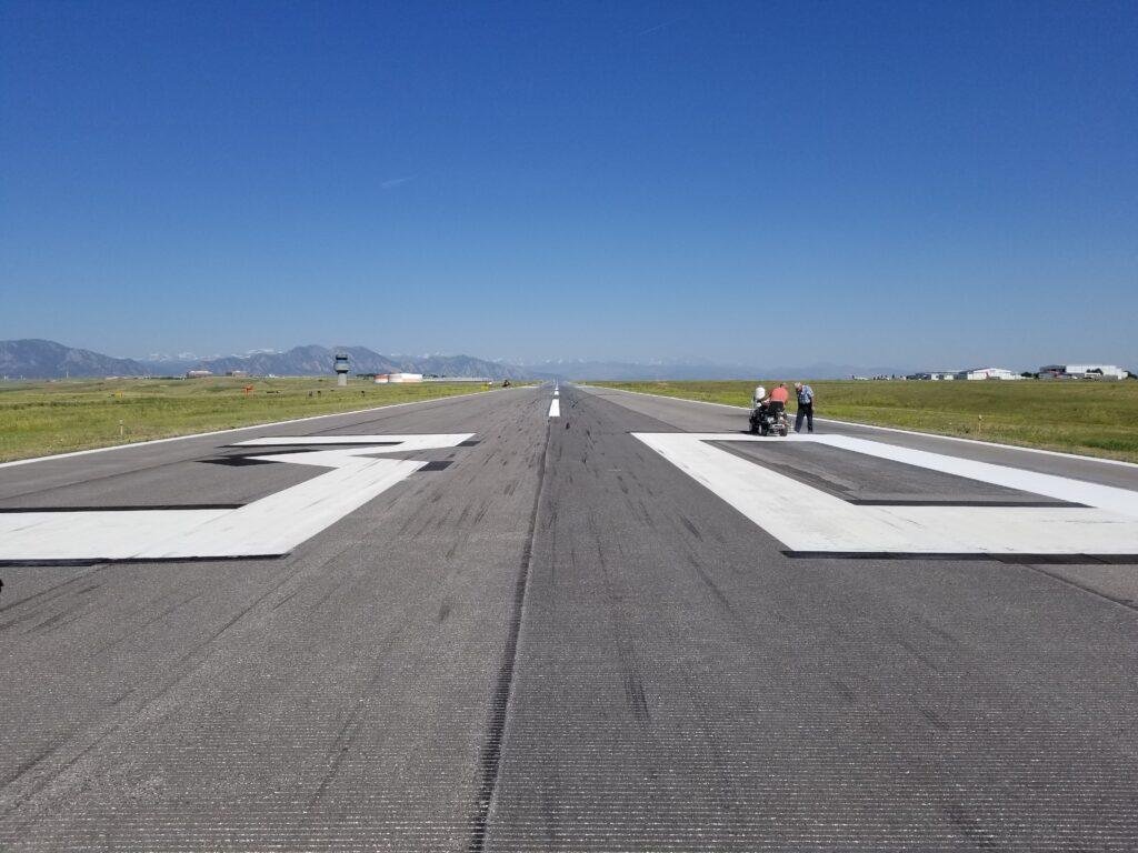 Workers painting white runway designation numbers at Rocky Mountain Metropolitan Airport