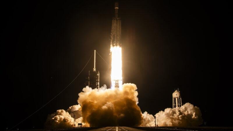 Falcon Heavy rocket lifting off at night on the NROL-97 mission, with a bright exhaust plume and clouds of smoke over Launch Complex 39A