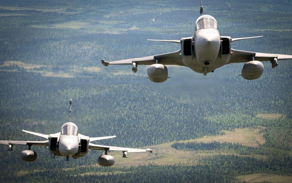 Gripen engine cooperation illustrated by two Saab JAS 39 Gripen fighter jets flying in formation above a forested landscape.