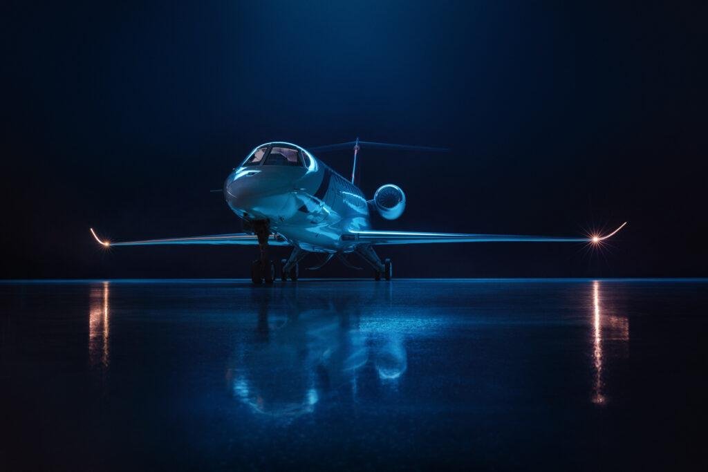 SyberJet SJ36 business jet viewed from the front under blue lighting inside a dark hangar.