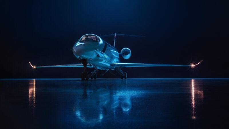 SyberJet SJ36 business jet viewed from the front under blue lighting inside a dark hangar.