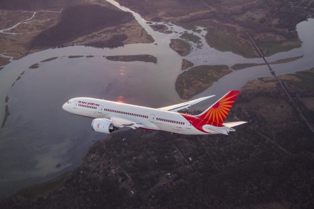 Air India fuel surcharge article illustrated by an Air India Boeing 787 Dreamliner flying above a river and forested landscape.