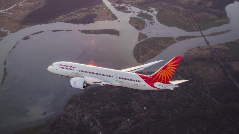 Air India fuel surcharge article illustrated by an Air India Boeing 787 Dreamliner flying above a river and forested landscape.