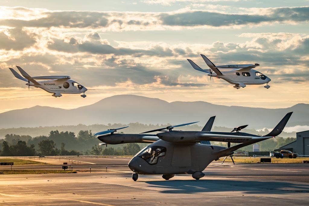 BETA Technologies A250 and CX300 electric aircraft flying above an airfield at sunset, with another aircraft on the ground