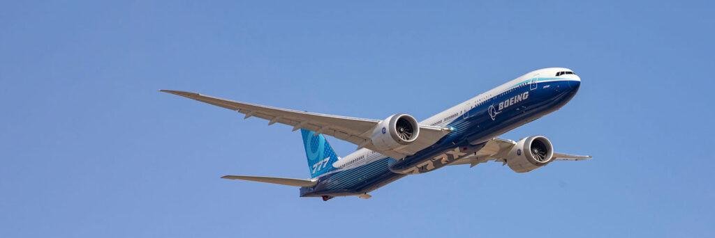 Boeing Hutchinson Partnership illustrated by a Boeing 777X widebody aircraft flying against a clear blue sky in Boeing's blue test-aircraft livery.