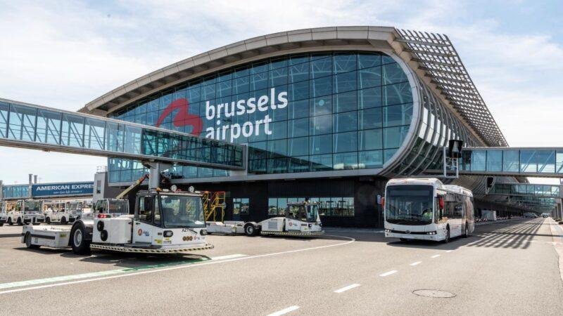 Brussels Airport strike article illustrated by the airport's glass-fronted passenger terminal, ground service vehicles, and airport shuttle bus.