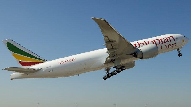 Ethiopian Airlines cargo Boeing 777 freighter, registration ET-APS, taking off with its landing gear extended against a clear blue sky.