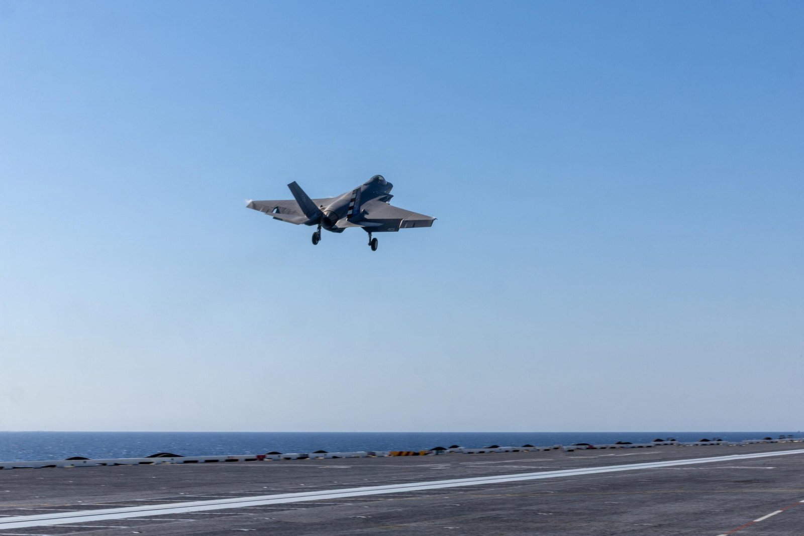 F-35C Kennedy landing coverage: F-35C fighter airborne above a carrier deck during flight operations.
