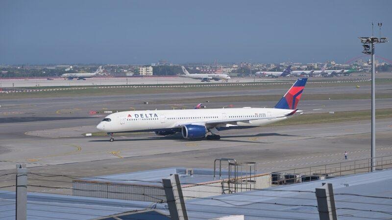 Delta Air Lines Airbus A350 in white livery with red and blue tail taxiing on an airport taxiway, with other airliners parked in the distance