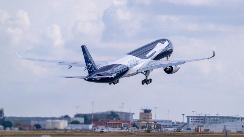 Lufthansa A350-1000 in special blue 100th-anniversary livery flying above an airport with landing gear extended.