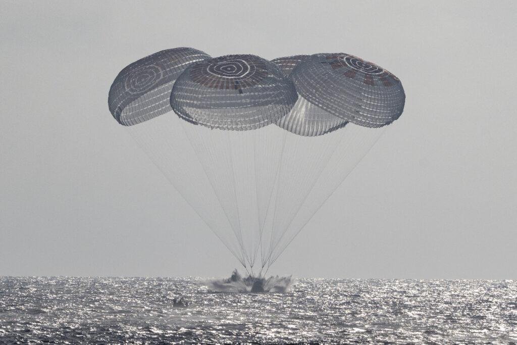 NASA Crew-12 return showing the SpaceX Crew Dragon Freedom spacecraft splashing down beneath parachutes in the Pacific Ocean off California.