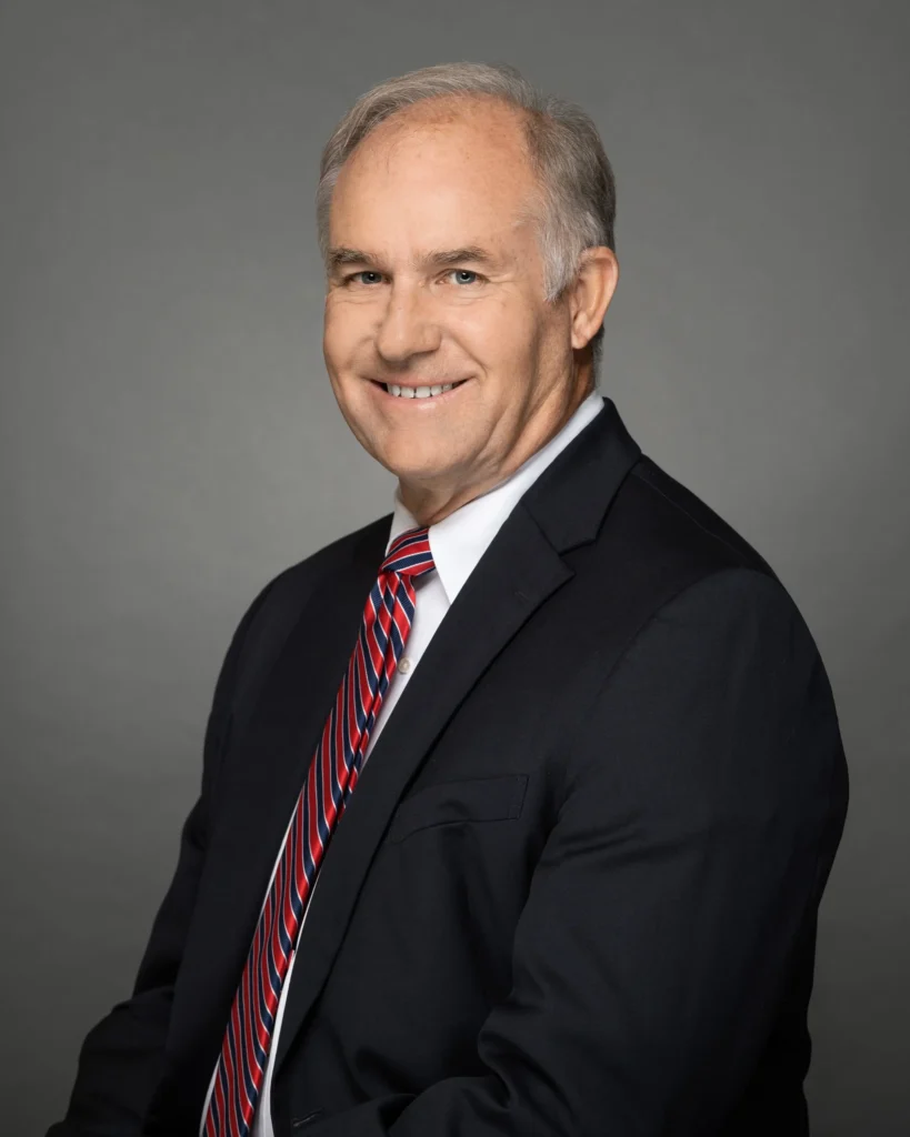 NASA Marshall Director Stephen Cash pictured in a dark business suit and red-and-blue striped tie against a gray background.