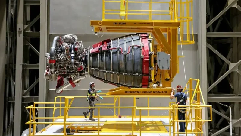 NASA technicians position an RS-25 rocket engine on a yellow horizontal installer during Artemis rocket assembly.