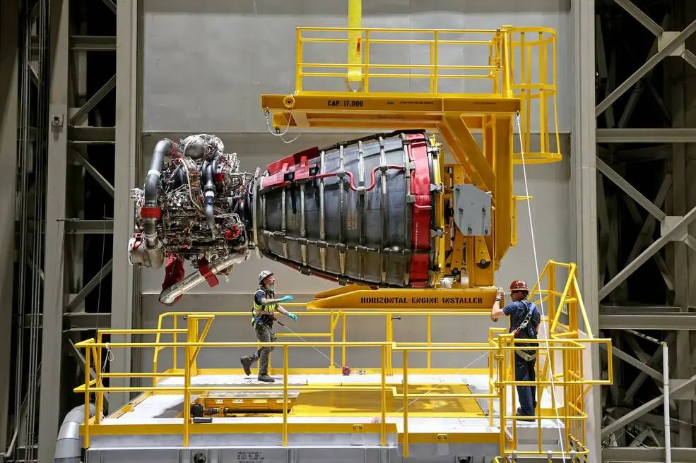NASA technicians position an RS-25 rocket engine on a yellow horizontal installer during Artemis rocket assembly.