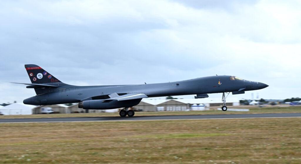 B-1B Lancer touching down on a runway under a grey sky, with 80th anniversary tail art