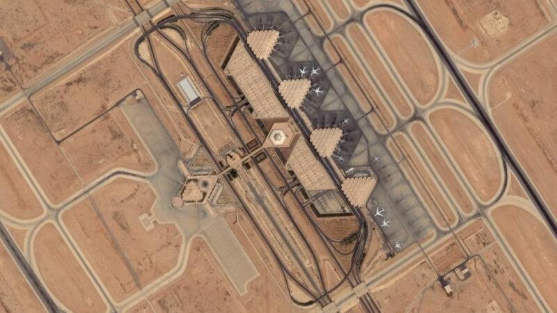 Riyadh flight cancellations illustrated by an aerial satellite view of airport terminals, parked aircraft, taxiways, and surrounding aviation infrastructure.