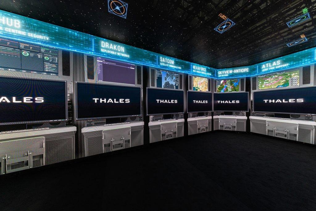 Thales aerospace and defense technology exhibition display with screens showing radar, satellite communications and air-defense systems.