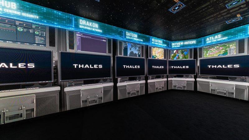 Thales aerospace and defense technology exhibition display with screens showing radar, satellite communications and air-defense systems.